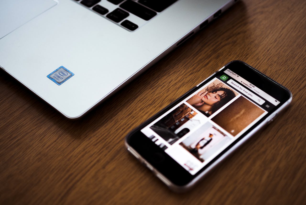 Smartphone displaying photos next to a laptop on a wooden desk, highlighting modern technology.